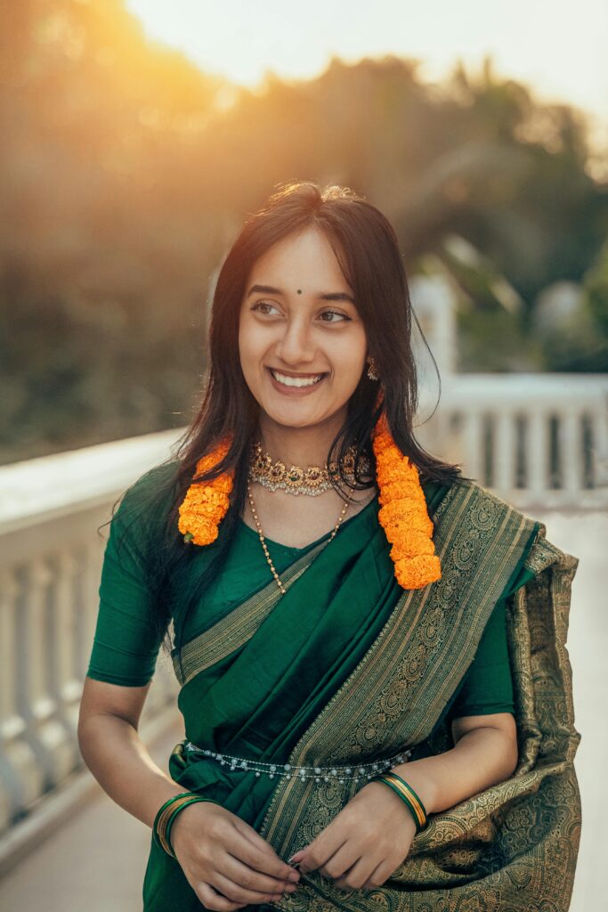 A young woman in a green saree with floral adornments, outdoors during sunset.